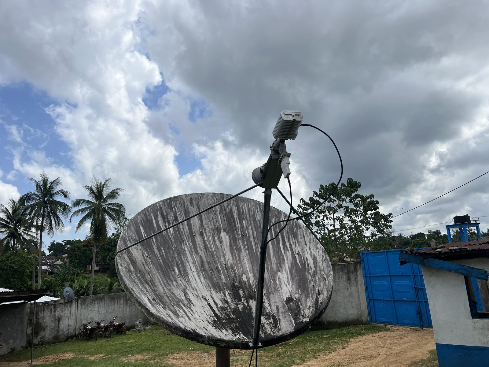 Satellite antenna with its feed, BUC and LNB at the Plan International field office in Bomi County, with palm trees and a compound wall behind
