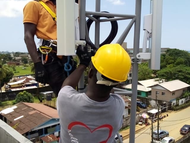 Deux ingénieurs en harnais de sécurité installant des antennes sectorielles sans fil sur un pylône surplombant Monrovia