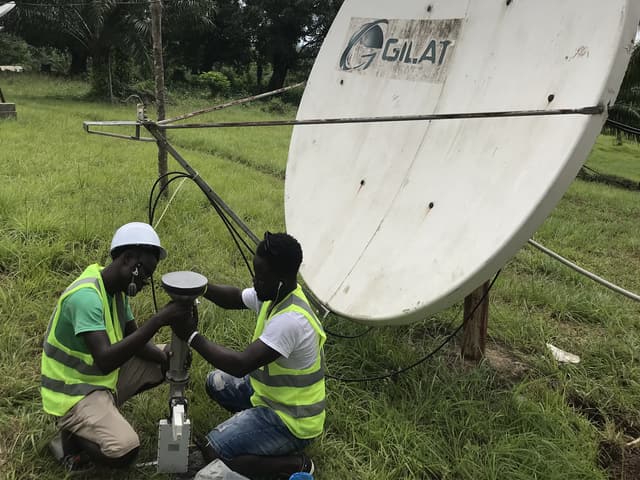 Deux ingénieurs en gilet haute visibilité travaillant au pied d'une antenne bande C de 2,4 m sur le campus de l'université Tubman