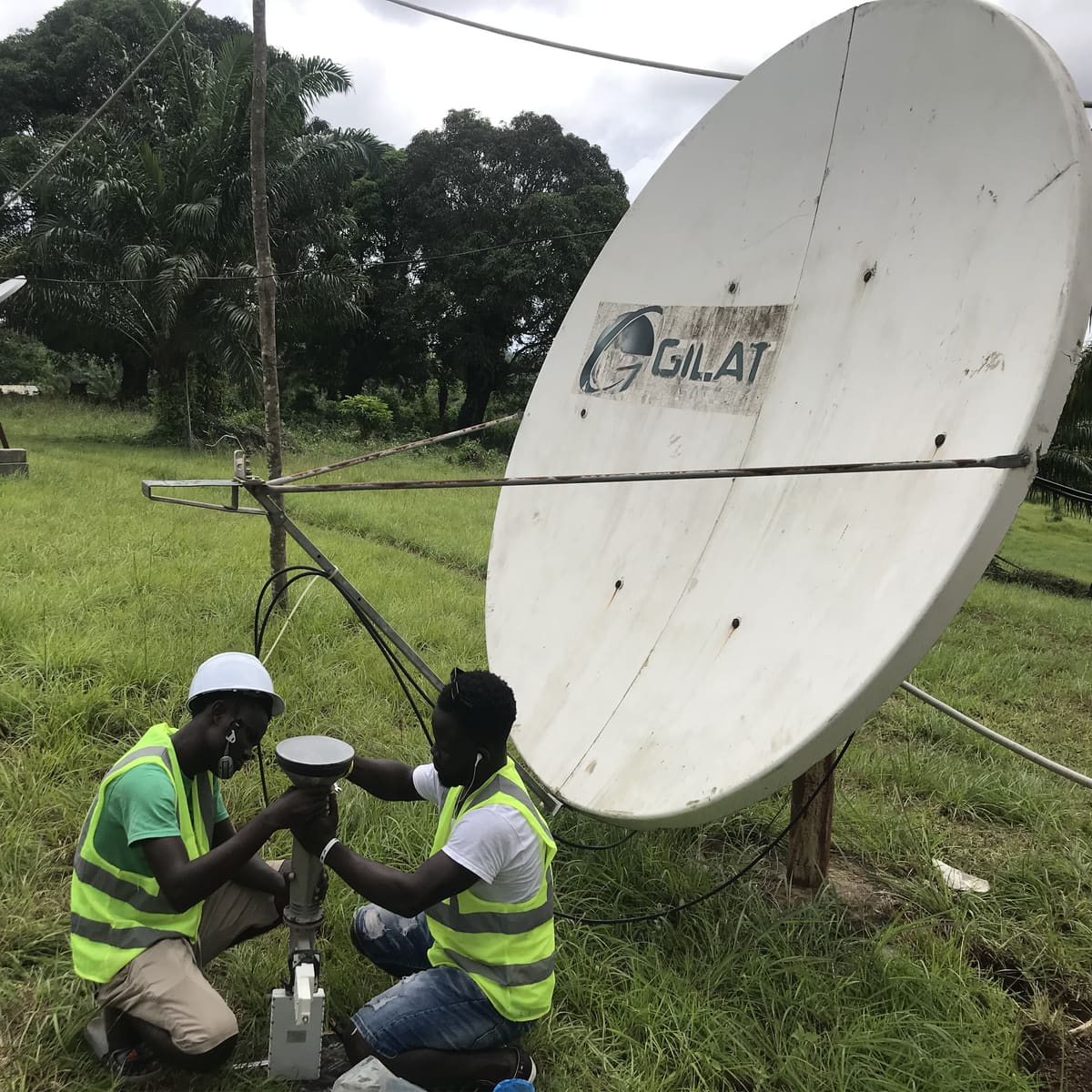 Deux ingénieurs de Global IT Firm en gilet haute visibilité travaillant au pied d'une antenne bande C de 2,4 m