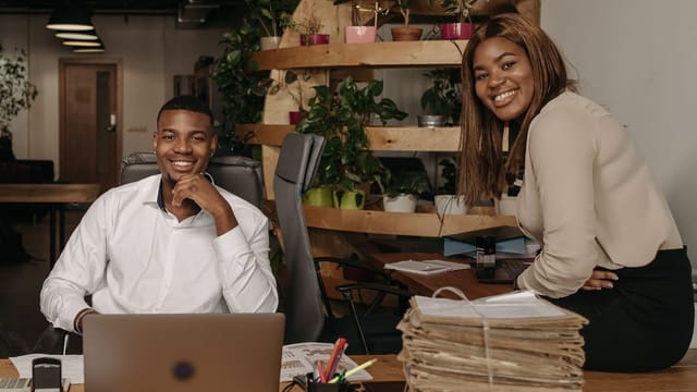 Deux collègues à leur bureau, à côté d’une haute pile de dossiers papier