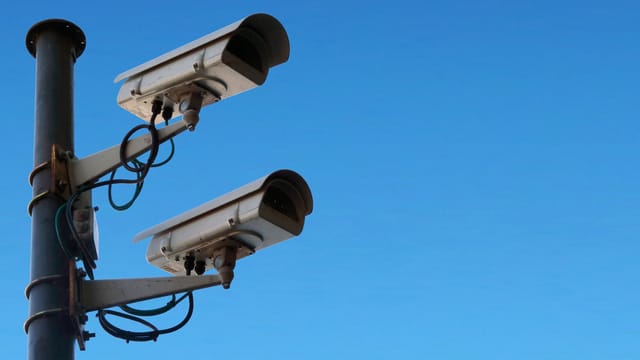 Two outdoor CCTV cameras mounted on a pole against a clear blue sky
