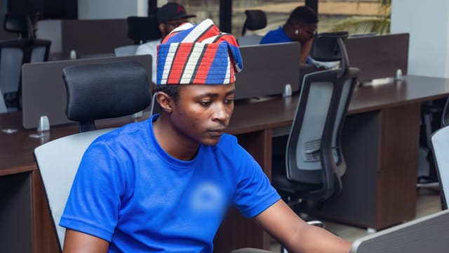 Jeune développeur coiffé d'un bonnet à motifs, travaillant sur un ordinateur portable dans un open space