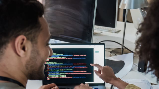 Two developers reviewing code together on a laptop screen