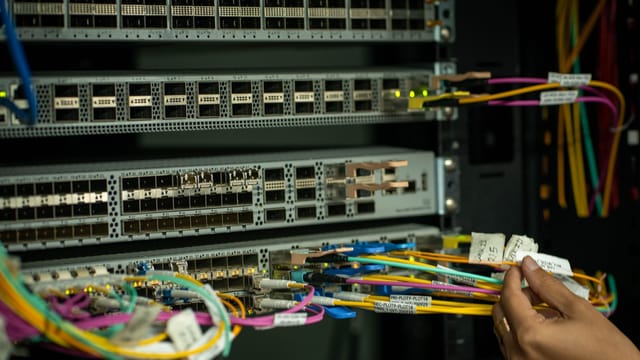 Hand connecting colour-coded fibre patch cords to network switches in a server rack