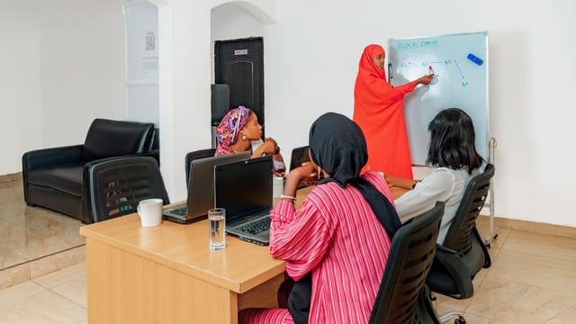 Formatrice au tableau blanc devant un petit groupe de femmes équipées d'ordinateurs portables