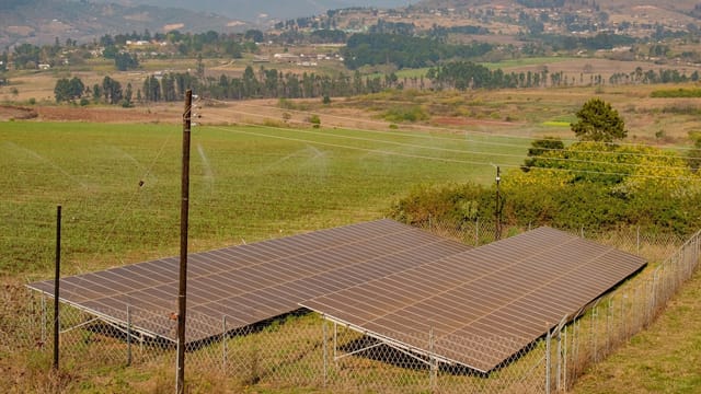 Ground-mounted solar panel array behind a fence in a rural landscape