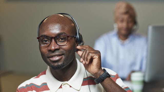 Smiling support agent with glasses adjusting a headset microphone in an office