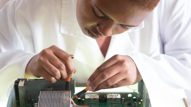 Technician in a lab coat working on a computer circuit board with precision screwdrivers