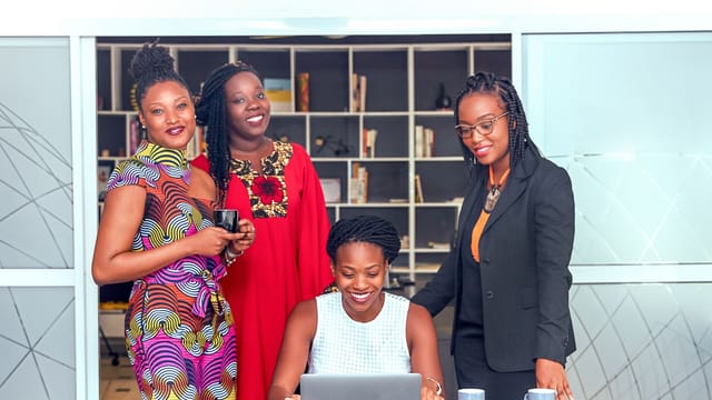 Quatre femmes réunies autour d'un ordinateur portable dans un bureau lumineux avec des étagères
