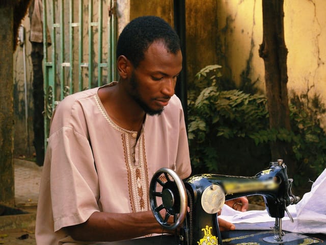 Tailor sewing white fabric on a manual sewing machine in Abuja, Nigeria