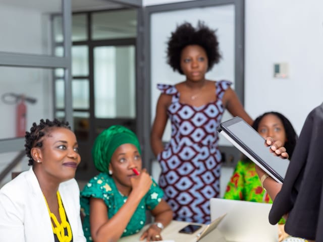 Team of women discussing work around a tablet in an office meeting