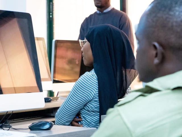 Formateur animant un cours devant des étudiants installés à des ordinateurs dans une salle informatique