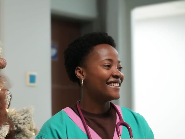 Smiling nurse in scrubs with a stethoscope in a hospital corridor