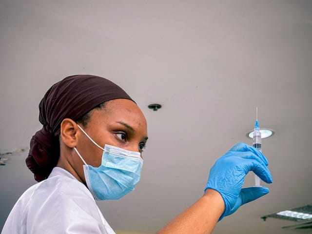 Health worker in a mask and gloves preparing an injection