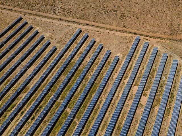 Aerial view of rows of ground-mounted solar panels on dry land