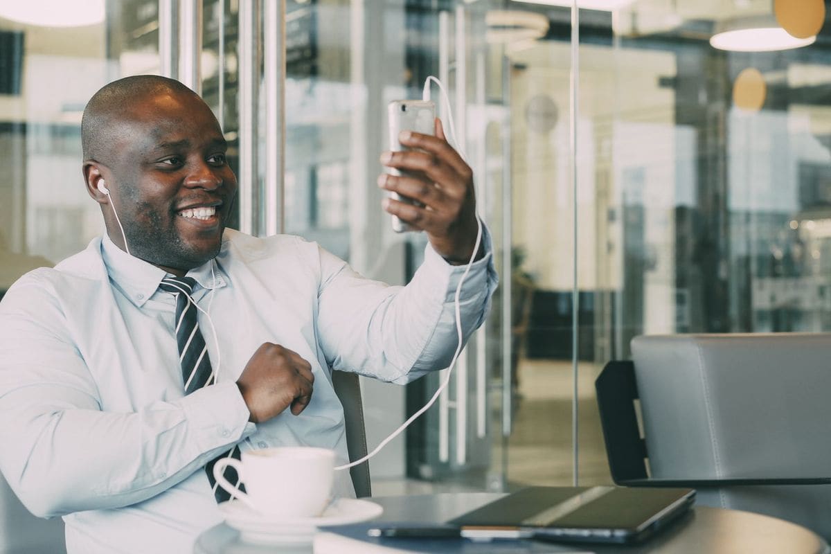 Professionnel souriant en appel vidéo avec un smartphone et des écouteurs dans un bureau