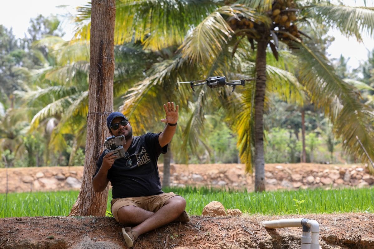 Homme pilotant un drone équipé d'une caméra avec une télécommande dans un champ tropical