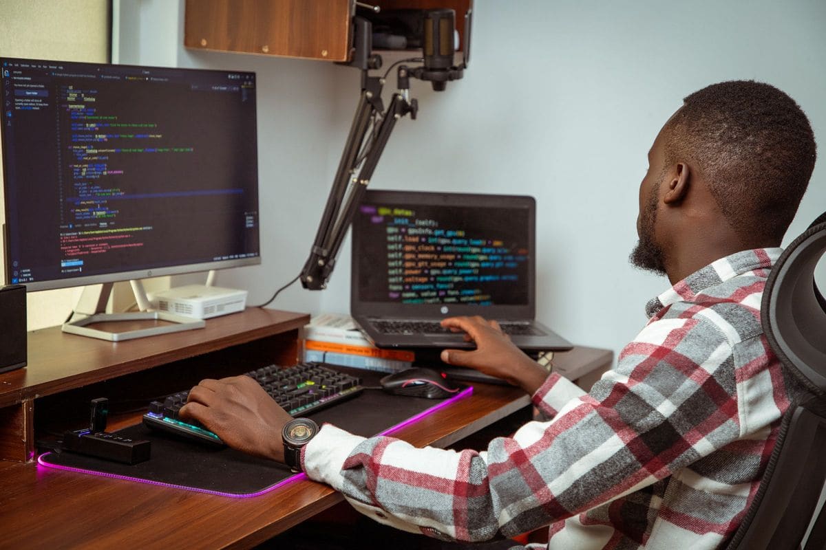 Développeur écrivant du code sur un écran de bureau et un ordinateur portable dans un bureau